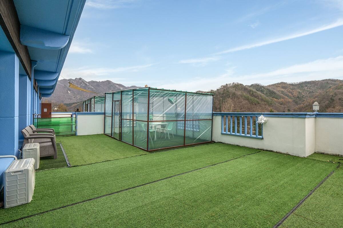 Une terrasse sur le toit avec un revêtement d’herbe artificielle, une structure fermée par des parois de verre et une vue sur les montagnes.