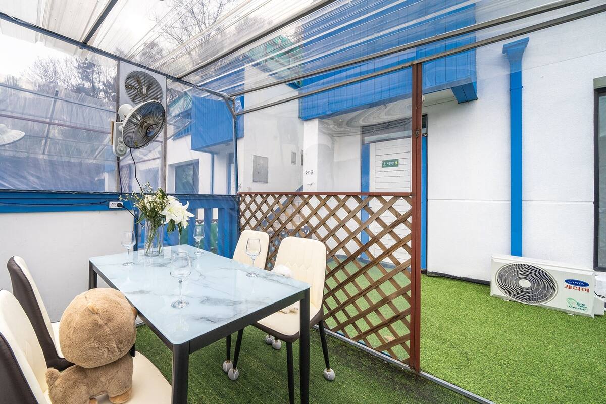 Un espace extérieur abrité, aménagé pour prendre les repas, avec une table, des chaises et un ours en peluche.