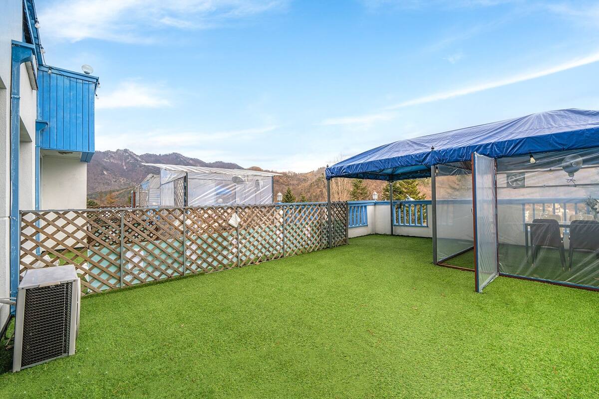 Une terrasse sur le toit avec un revêtement d’herbe artificielle, un espace salon couvert et une vue sur les montagnes.