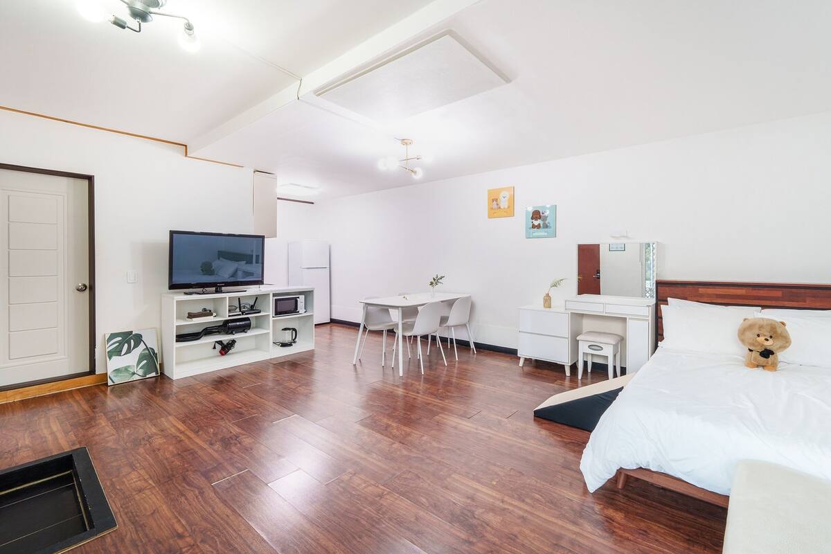Une chambre d’hôtel avec un plancher en bois, un lit, un bureau, une télévision, une petite table et une chaise.