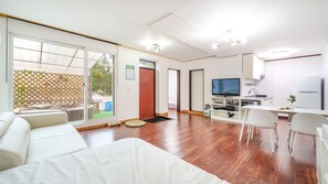 A modern living room with a sofa, a dining table, and a TV. There is a sliding glass door leading to a balcony. - Chuncheon Dogandstay (Chuncheon)