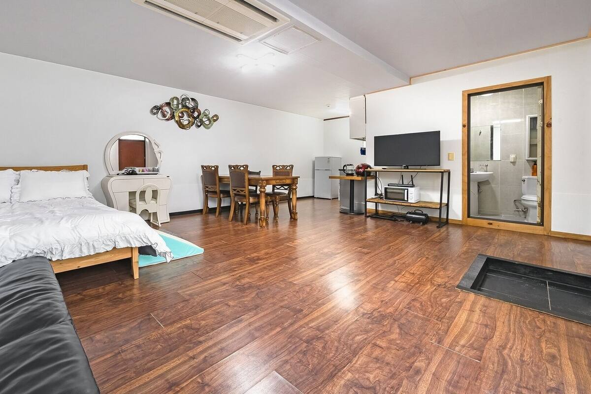 Une chambre à coucher comprenant un lit, un bureau, une chaise, un téléviseur et une salle de bain visible à travers une porte en verre.