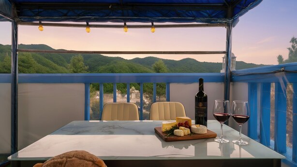 Una mesa dispuesta con queso, vino y una botella en un balcón con vistas a colinas verdes.