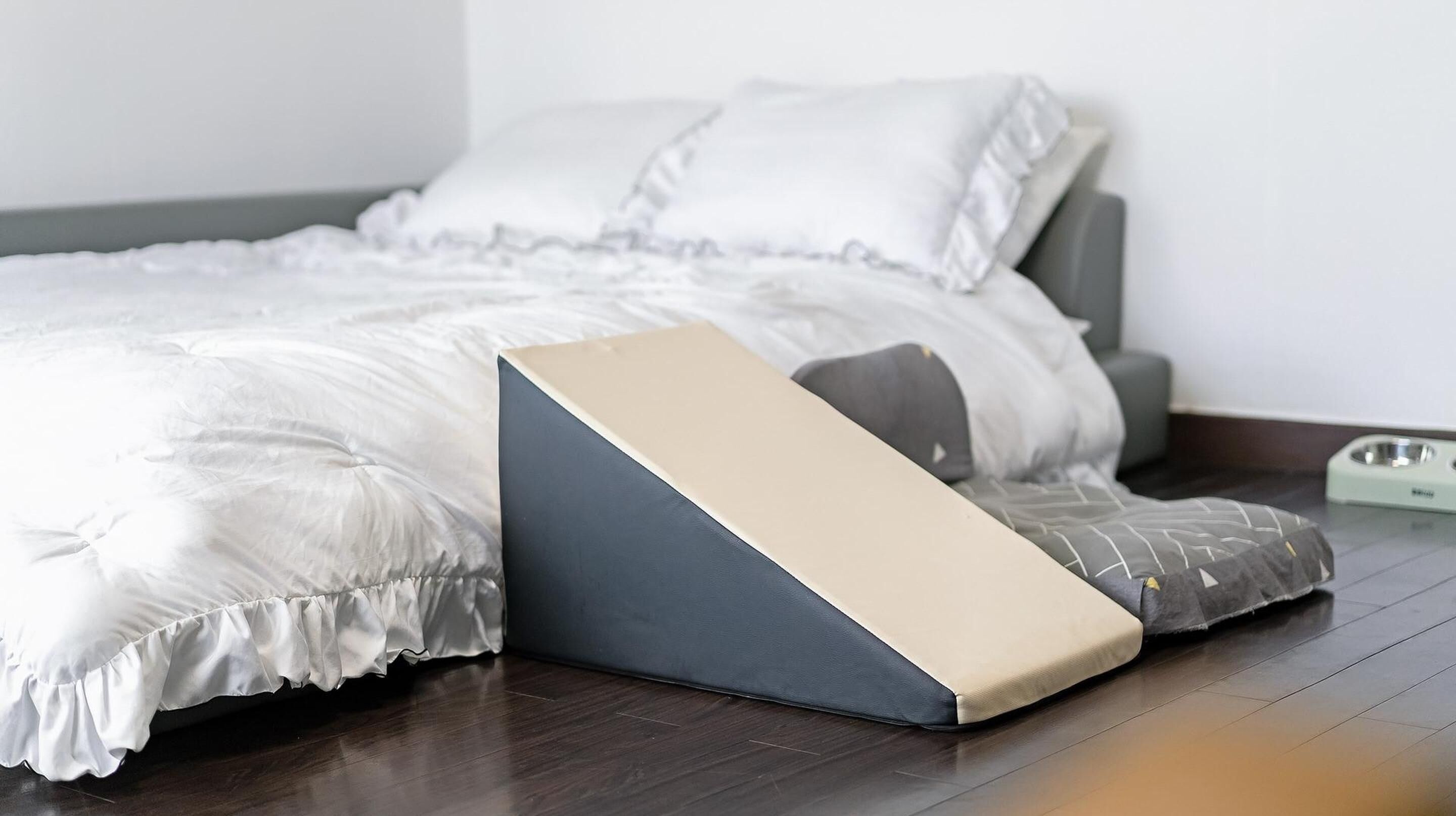 Un lit avec un surmatelas, un panier pour animal de compagnie et un bol d’eau posé sur le sol.