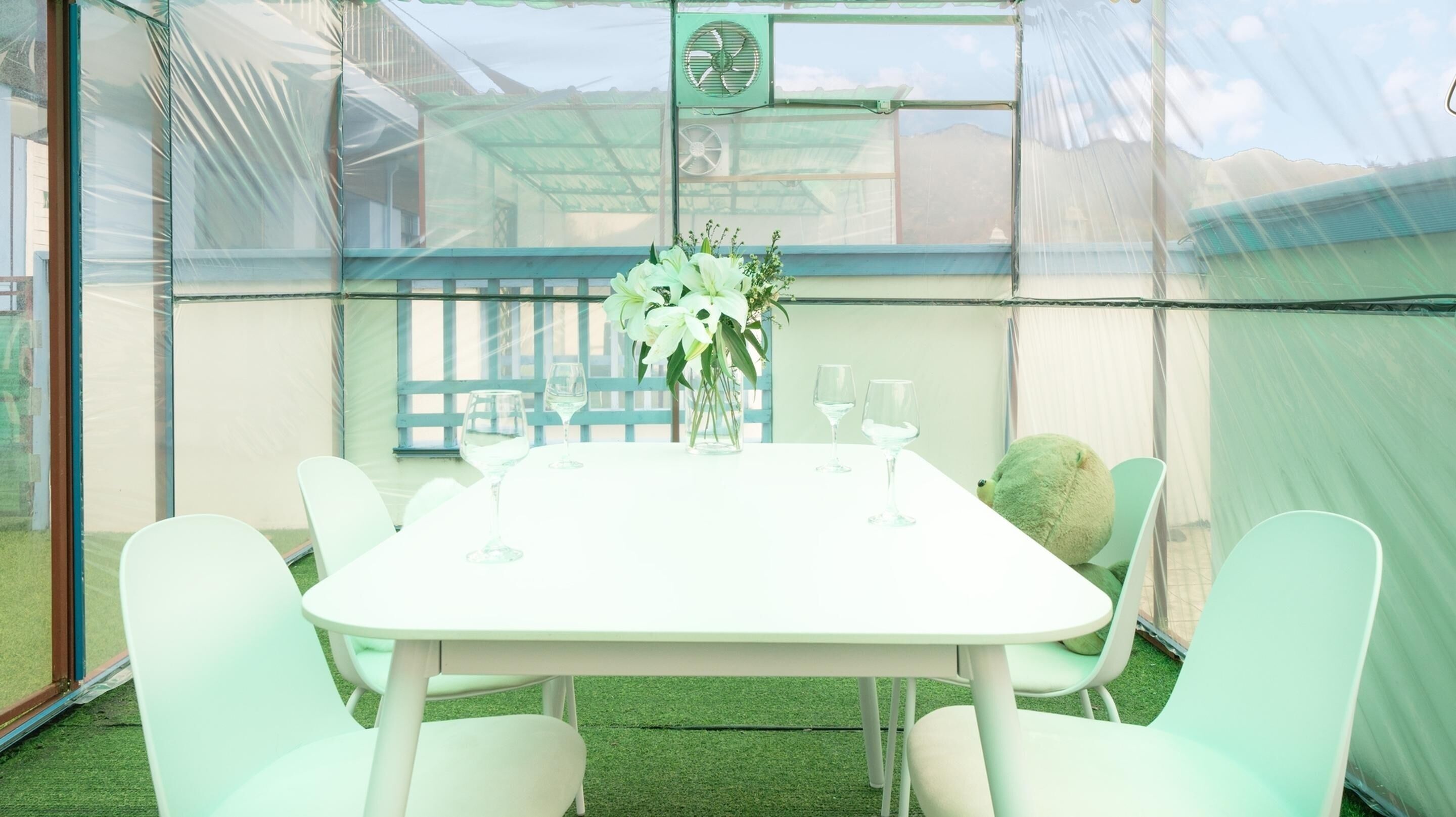 A table set for two with a vase of flowers, two wine glasses, and a teddy bear on the table.