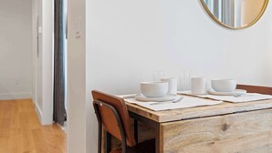 Un coin repas avec une table en bois, des assiettes blanches, des bols et un miroir au mur.