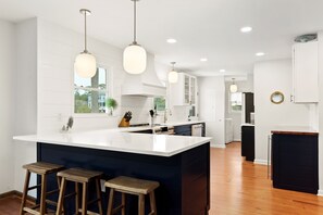 Una cocina moderna con una isla grande, taburetes de bar, lámparas colgantes y vistas al exterior.