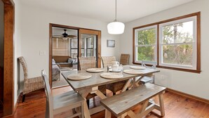 Un comedor con una mesa de madera, individuales tejidos, sillas de mimbre y una lámpara colgante.