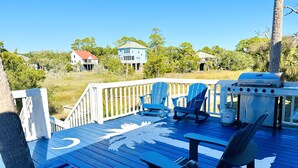 Una terraza con sillas Adirondack azules, una parrilla y vistas a casas y árboles.