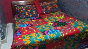 Una cama con una colcha y almohadas estampadas de flores en una habitación con paredes rojas y papel tapiz decorado.