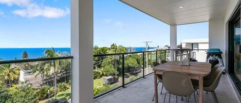 A balcony with a view of the ocean, a table with chairs, and a car parked outside.