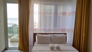 Una habitación de hotel con cama, cortinas y vista al mar.