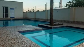 Una piscina con solárium empedrado, una palmera y un edificio blanco con cúpula y minarete al fondo.