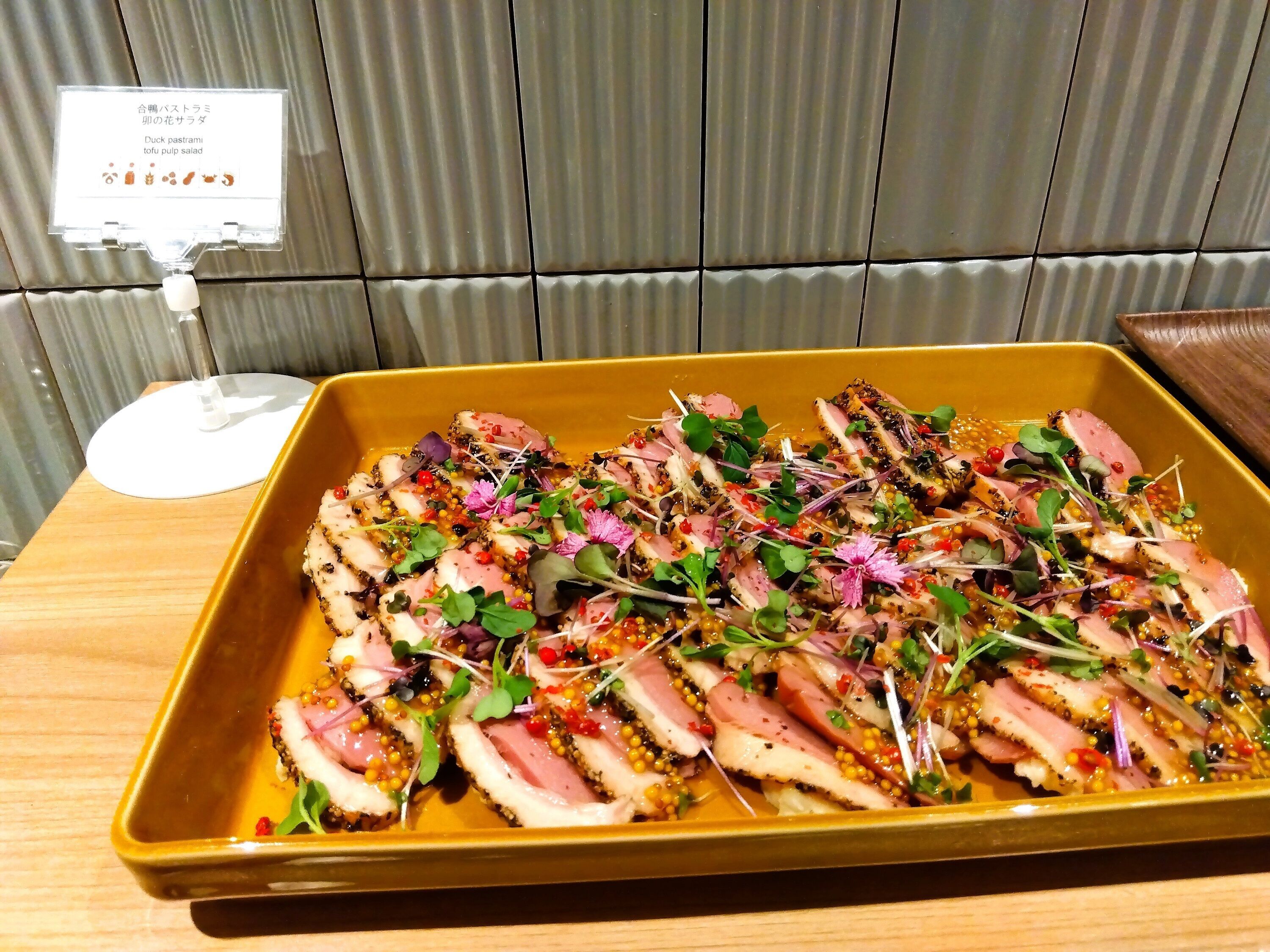 A dish of duck pastrami tofu salad in a yellow rectangular dish on a wooden table.