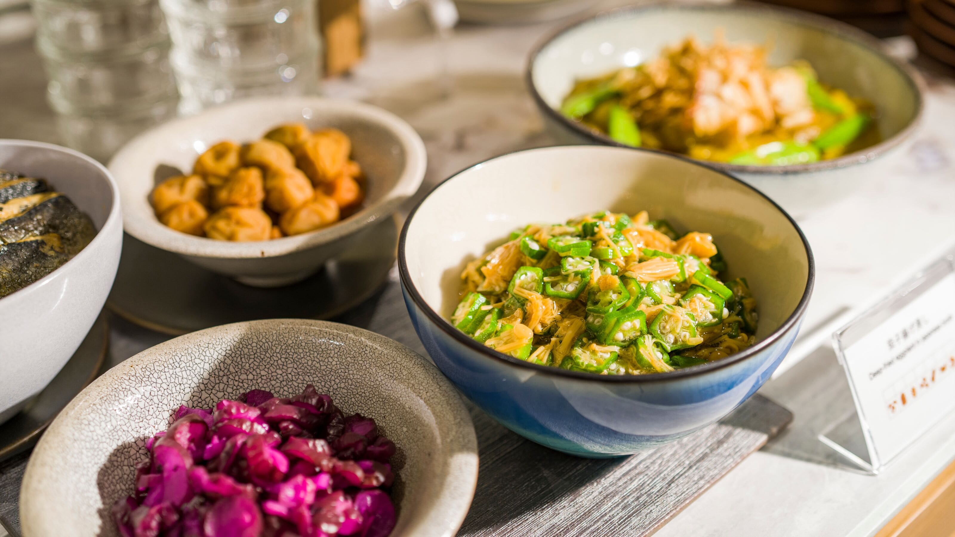 Uma mesa com diversos pratos, incluindo uma tigela de vegetais verdes, uma tigela de vegetais roxos e uma tigela de macarrão.