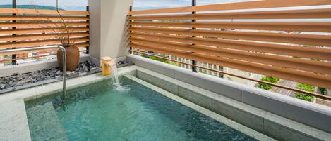 A rooftop pool with clear water, wooden slatted railings, and a view of buildings in the background.