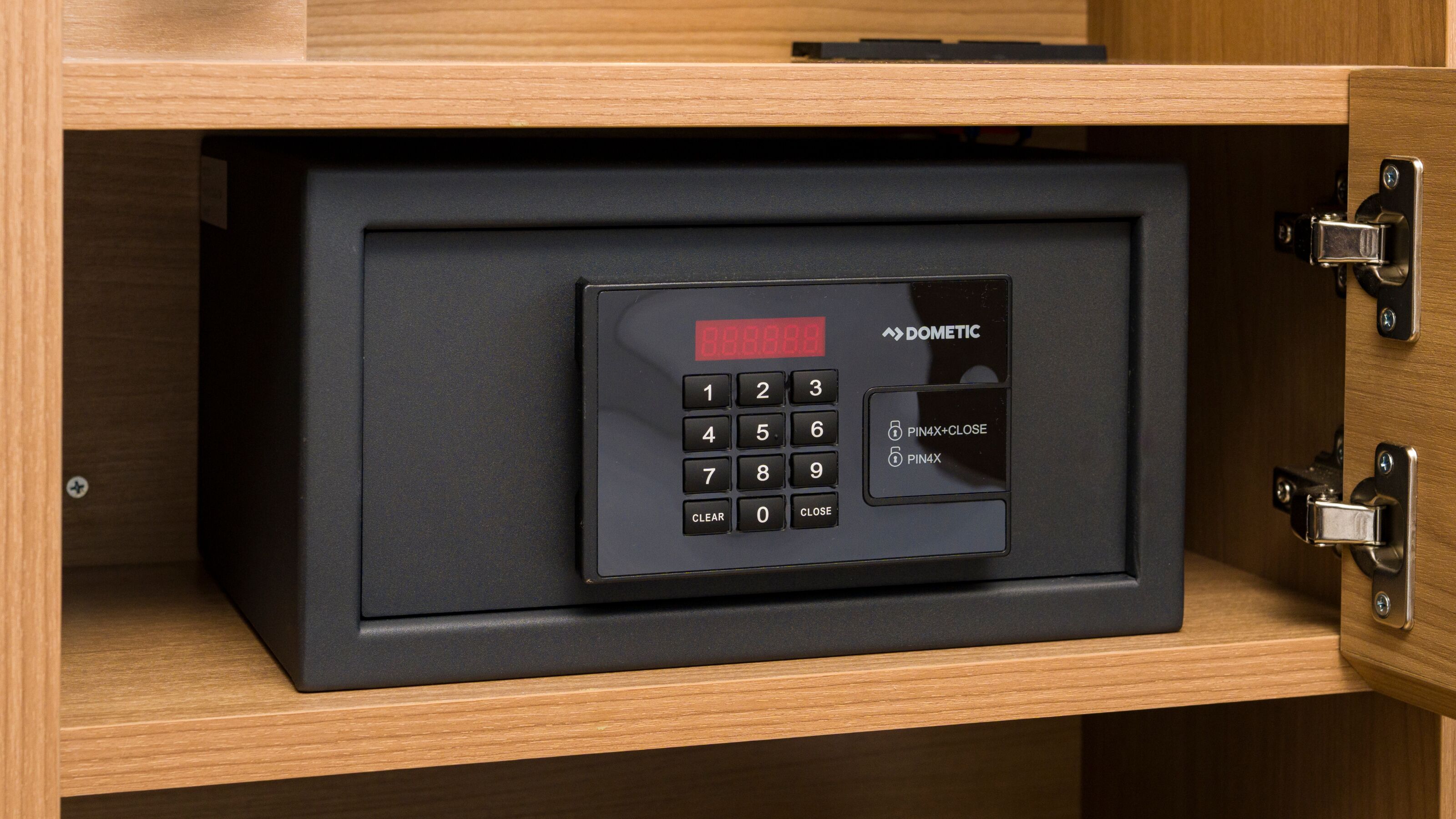 Un coffre-fort noir doté d’un clavier numérique et d’un écran, placé dans un meuble en bois muni d’un loquet métallique.