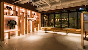 A modern interior with wooden shelving displaying various items, a bench area, and large windows offering a view of greenery outside.