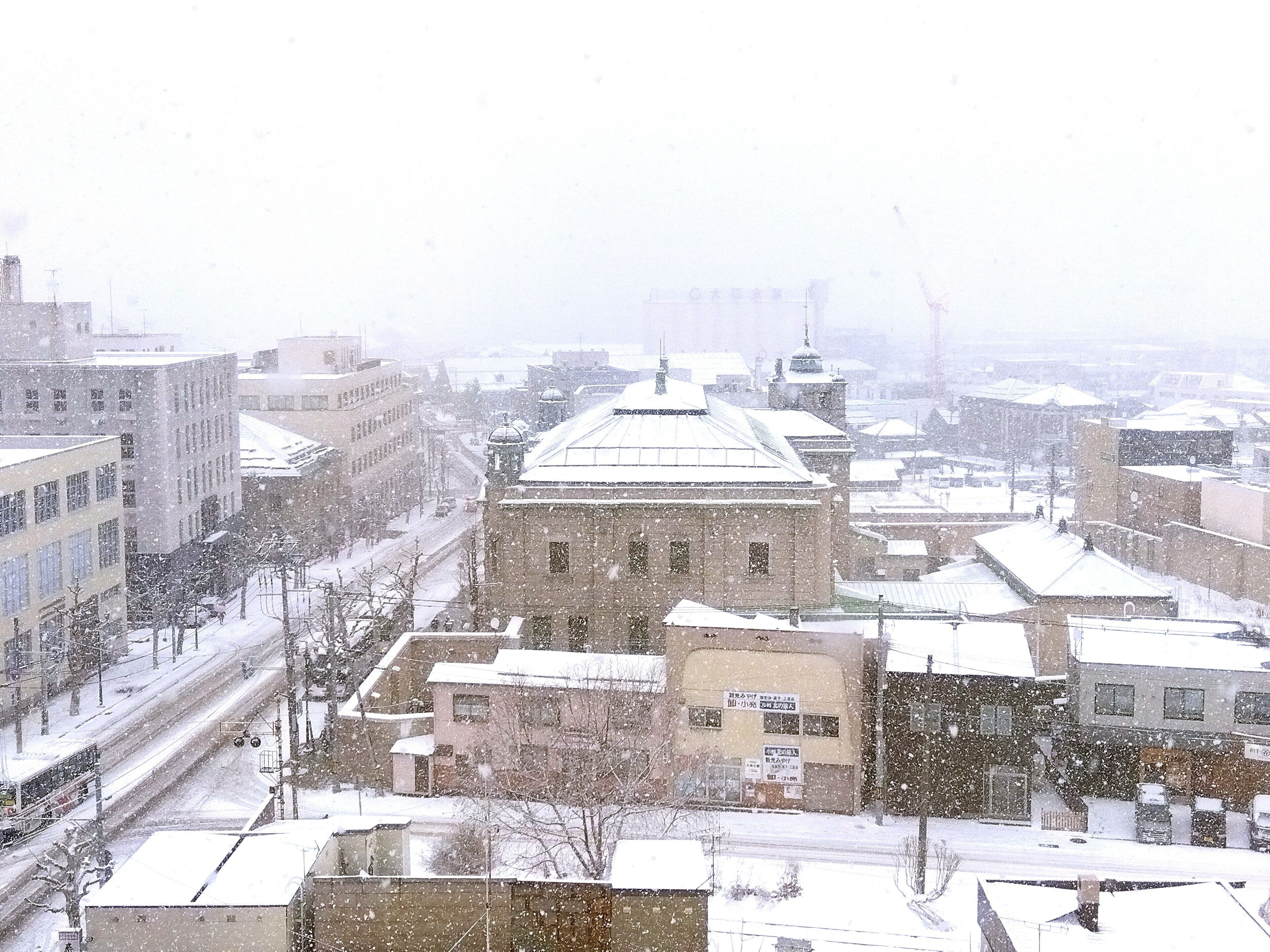 A snowy urban landscape with a prominent building featuring a dome and a clock tower.