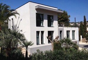 A modern two-story building with large windows and a flat roof, surrounded by greenery and palm trees. - Villa "Lynn" in Benissa Next to Mora with Mountain View, Pool & Wi-Fi (Benisa)