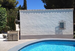 A swimming pool with a decorative edge, a wooden gate, and a building with a textured wall and a window. - Villa "Lynn" in Benissa Next to Mora with Mountain View, Pool & Wi-Fi (Benisa)