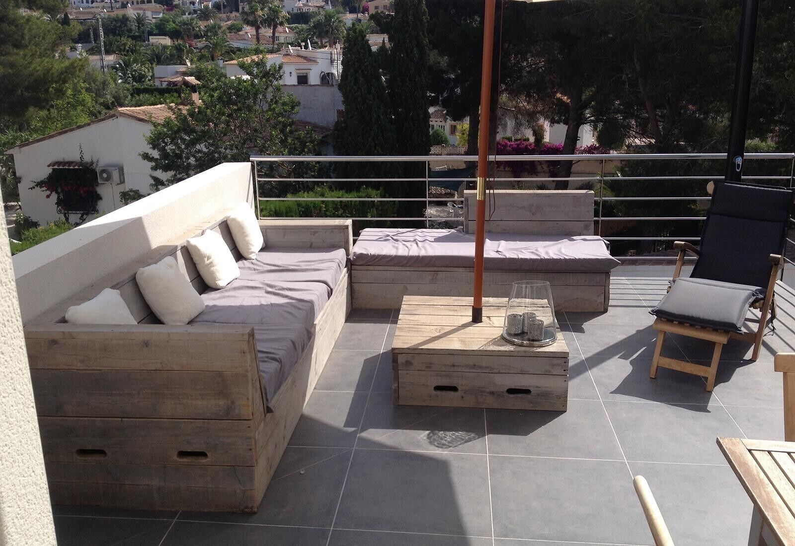 Eine Dachterrasse mit einer Holzsofa, einem Lounge-Sessel und einem kleinen Tisch mit einem Glasbehälter.