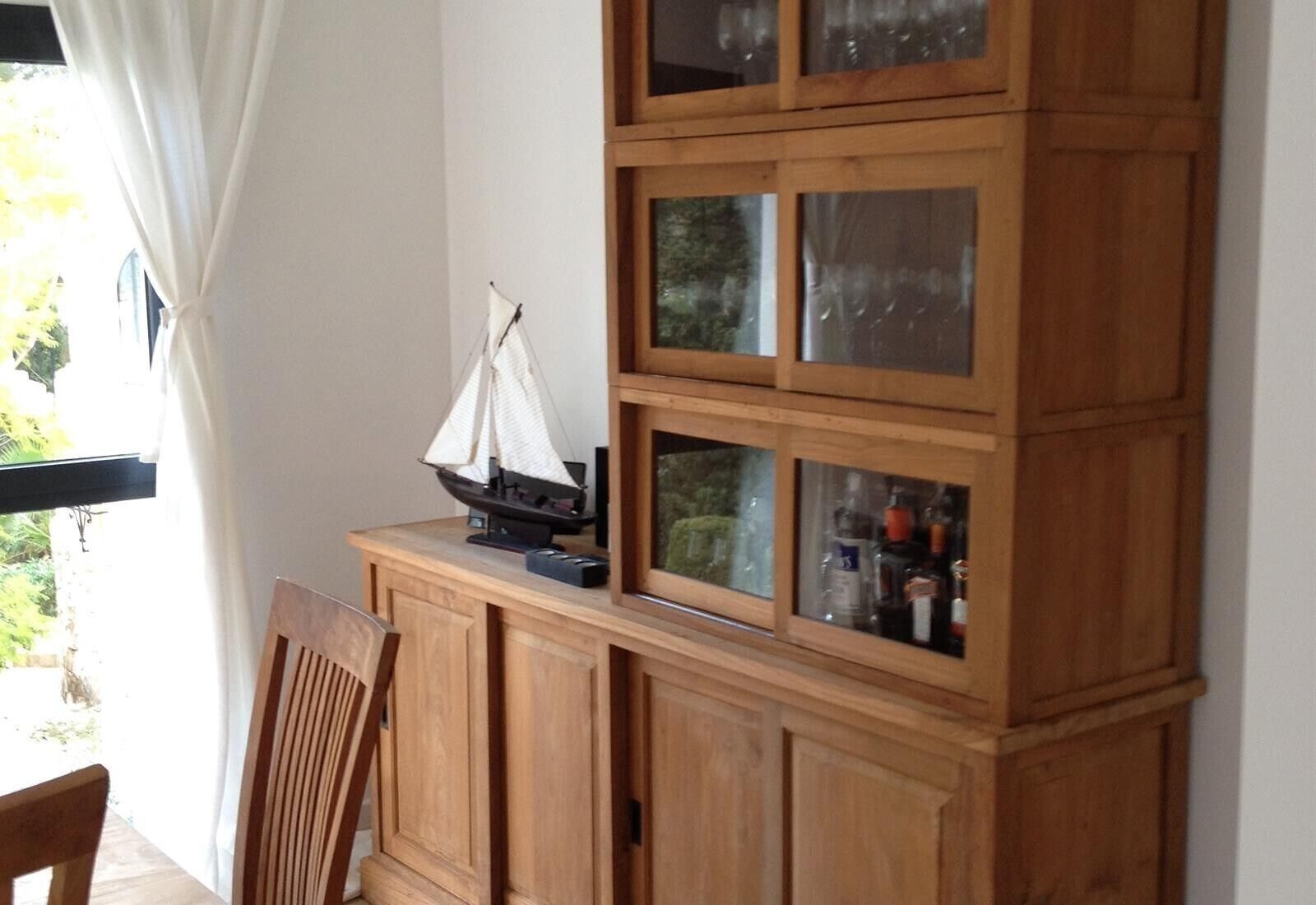 Un mueble de madera con puertas de vidrio, un velero en miniatura y una silla.