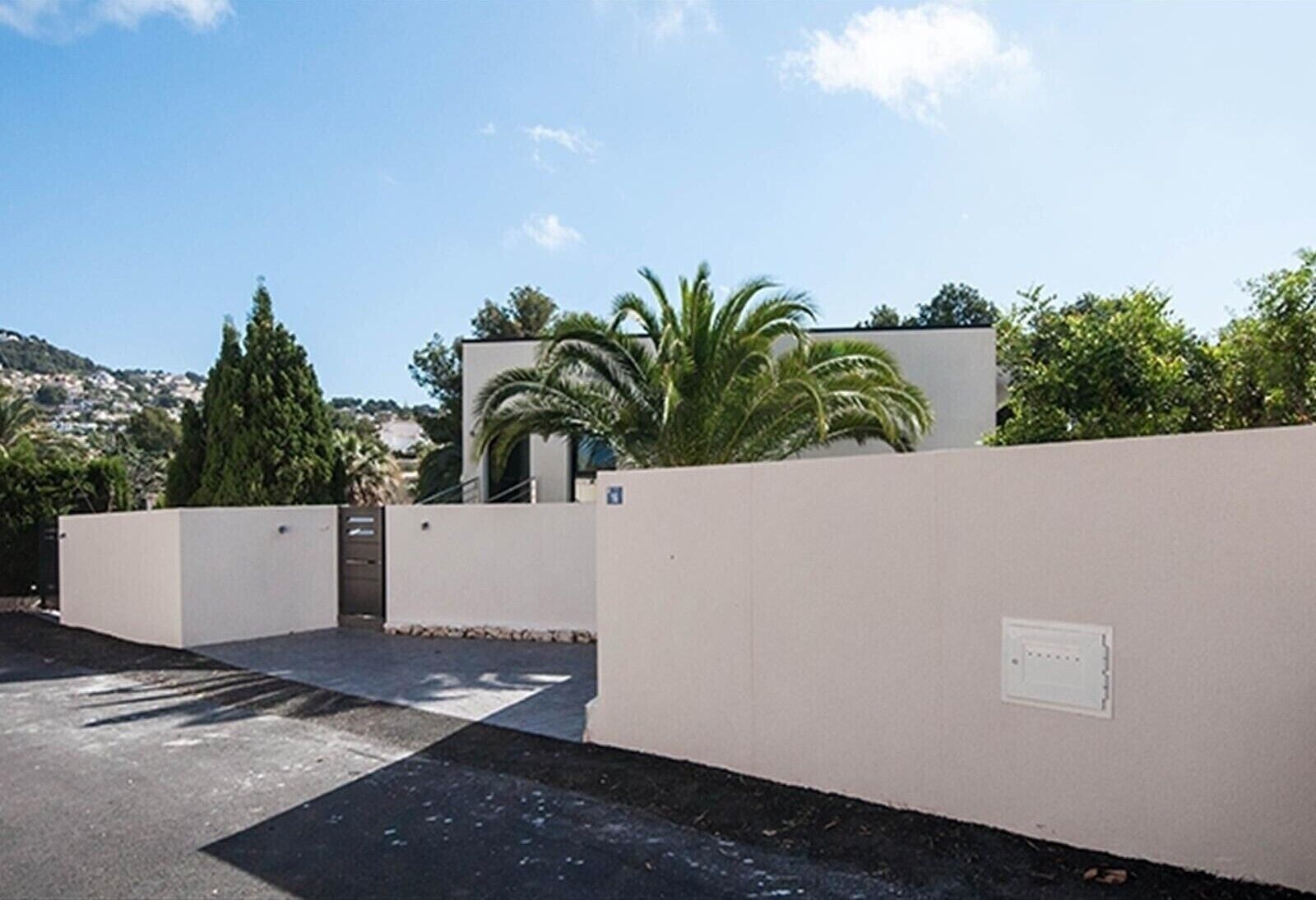 A modern building with a flat roof, white walls, and a paved entrance area.