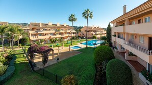 Un edificio residencial con piscina, palmeras y césped bien cuidado.