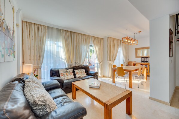 Una sala de estar moderna con un sofá de cuero, una mesa de centro de madera y un comedor con mesa y sillas.