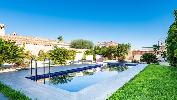 Una piscina con borde de baldosas, rodeada de césped y palmeras.