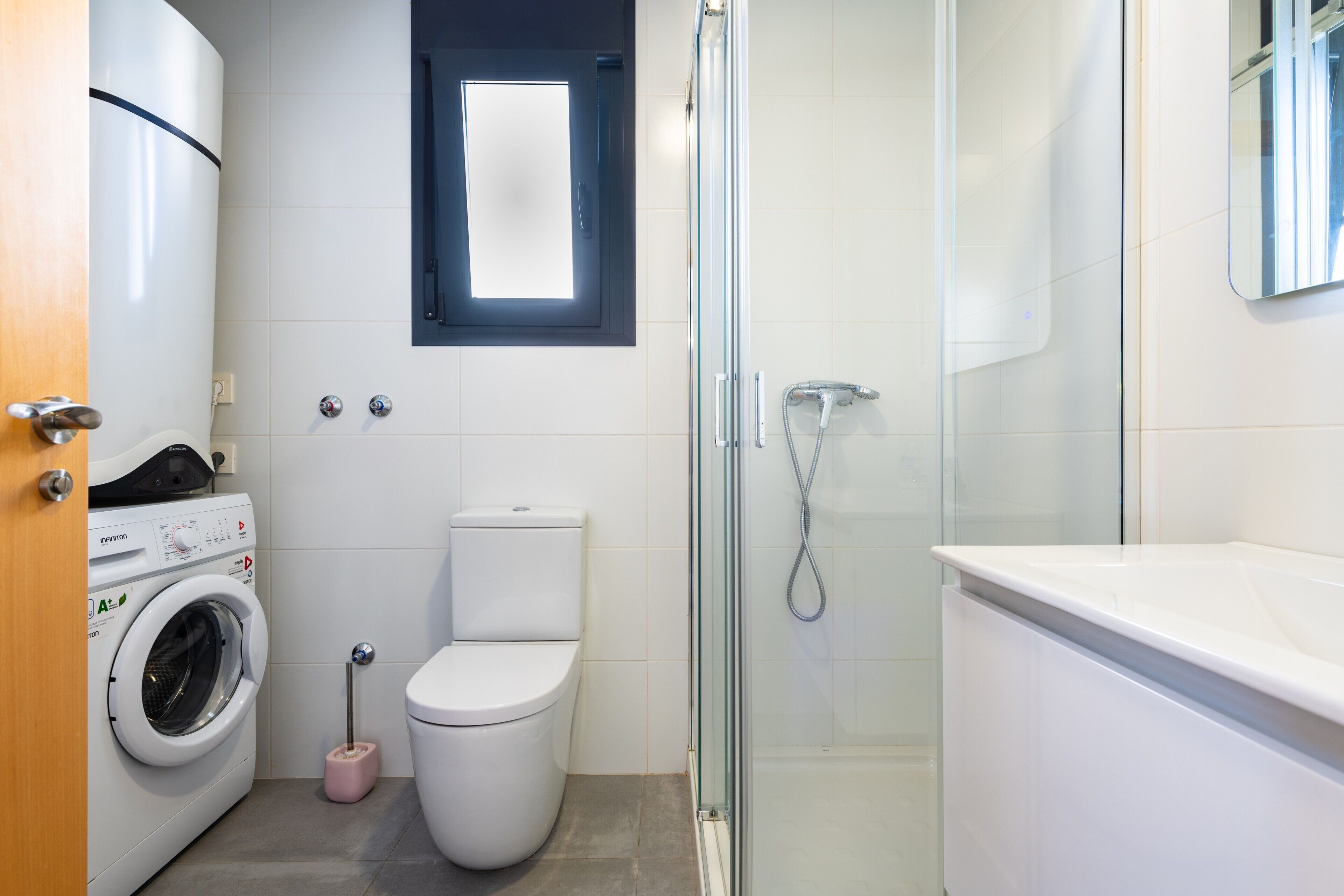 Une salle de bain moderne équipée d’un lave-linge, de toilettes, d’une douche à parois de verre et d’un grand miroir.