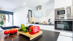 A modern kitchen with a black countertop, a wooden cutting board with vegetables, and stainless steel appliances. - Villa Puerto Blanco close to the Beach with Pool & Wi-Fi (Vinaròs)