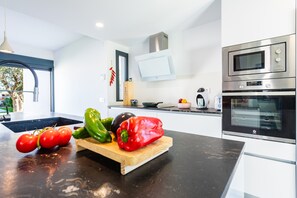 A modern kitchen with a black countertop, a wooden cutting board with vegetables, and stainless steel appliances.