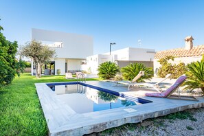 Un espace piscine extérieur moderne, doté d’une piscine à l’eau d’un bleu limpide, de chaises longues et d’une pelouse bien entretenue.