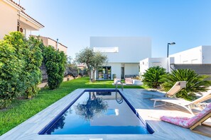 A modern pool area with a clear blue pool, lounge chairs, and a well-maintained lawn.