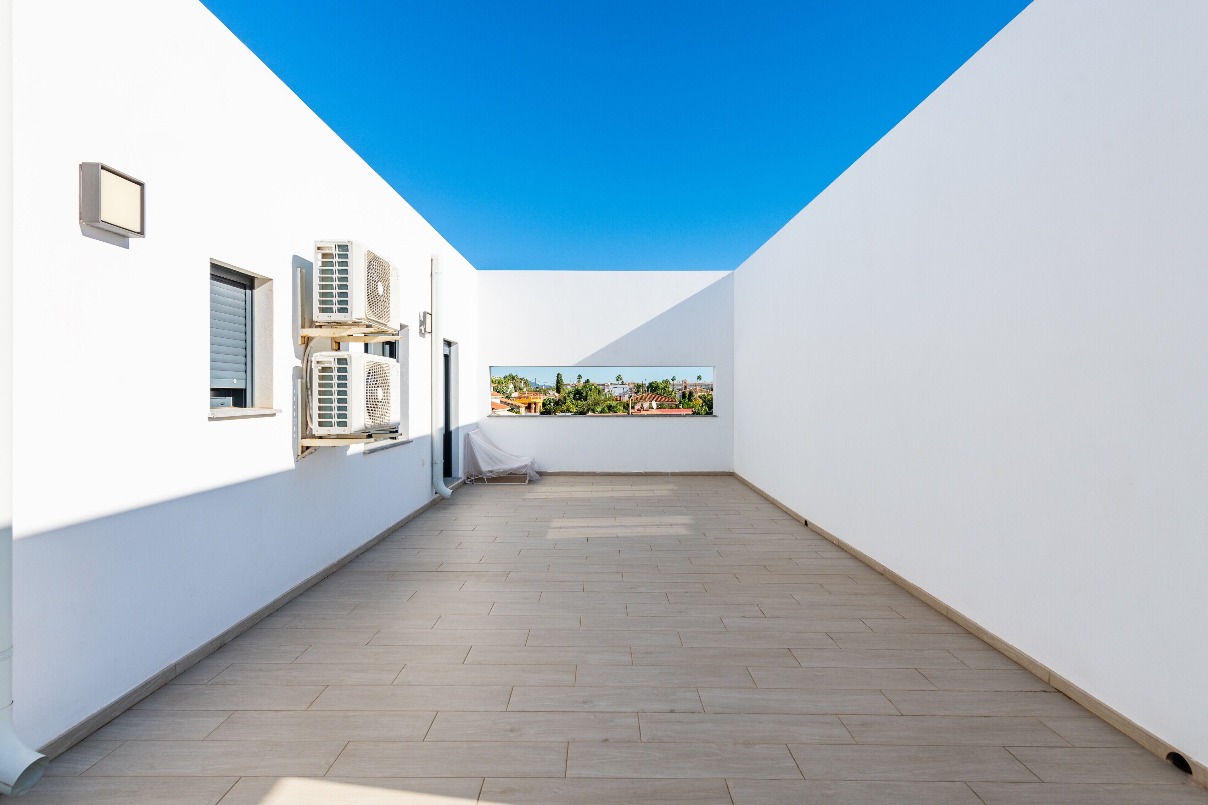 A rooftop terrace with a clear view of the city, white walls, and multiple air conditioning units.