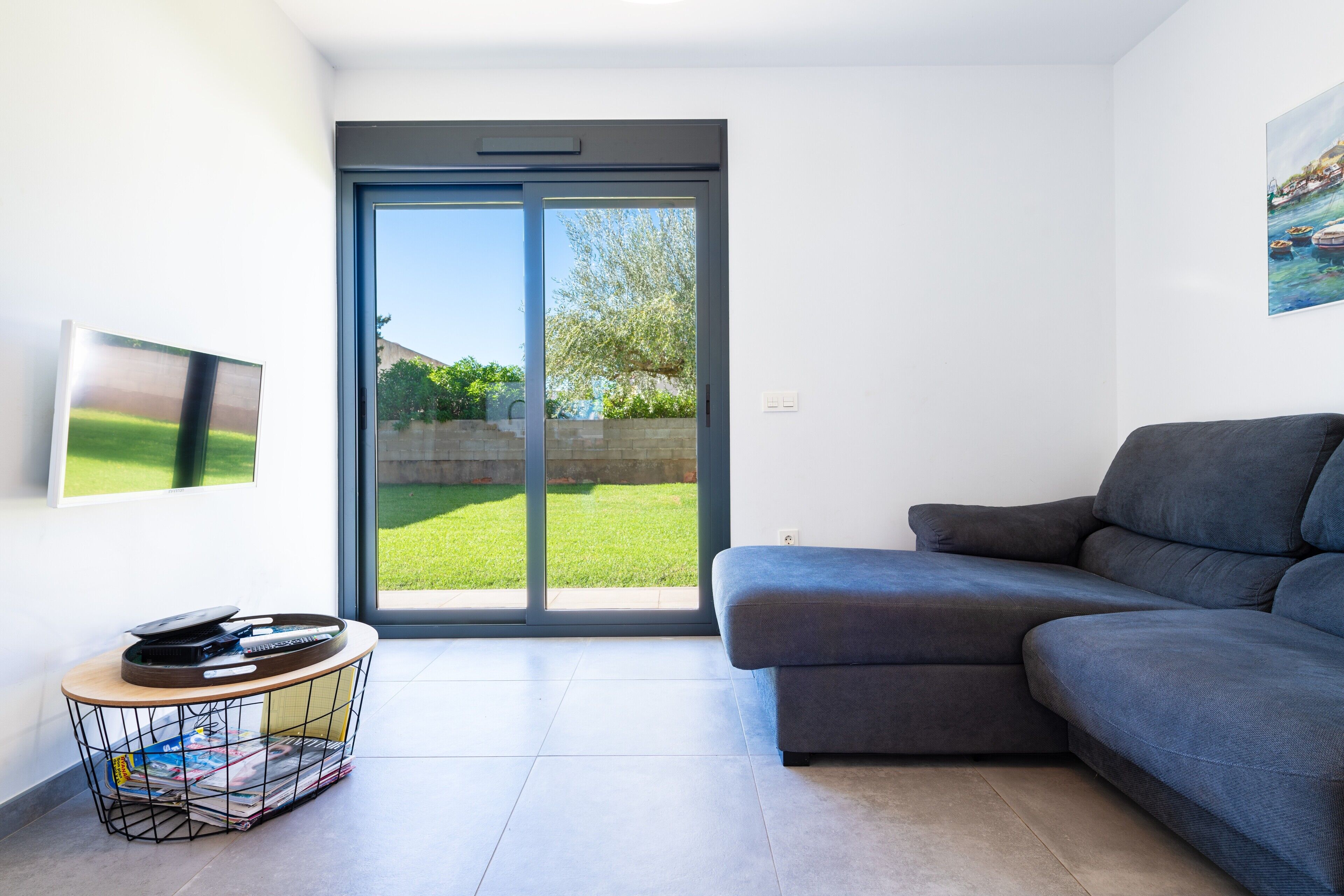 Ein modernes Wohnzimmer mit einem grauen Sofa, einem Couchtisch und einer Schiebeglastür, die in einen Garten führt.