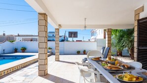 Un patio exterior con piscina, mesa de comedor, sillas y plantas en macetas.