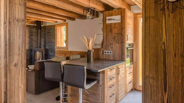A rustic kitchen with wooden beams, a bar area, and a stone fireplace.