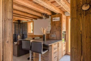 A rustic kitchen with wooden beams, a bar area, and a stone fireplace.