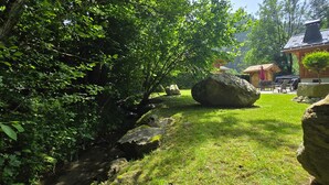 A grassy area with large rocks, a wooden structure, and dense foliage.