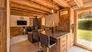 A rustic kitchen with wooden beams, a dining area with bar stools, a built-in oven, and a large sliding glass door to the outdoors.