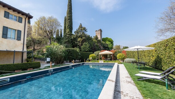 A swimming pool with lounge chairs, a gazebo, and a castle in the background.