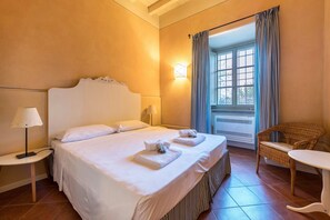 A hotel room with a large bed, two bedside tables, a chair, and a window with curtains.