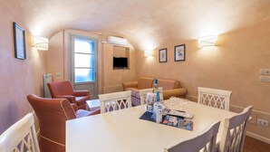 A room with a dining table, chairs, a sofa, a TV, and wall-mounted lights.