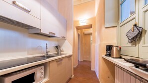 A compact kitchen with a microwave, stove, sink, and a hanging kettle.