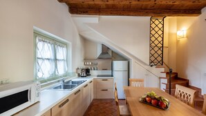 Une cuisine équipée d’un four à micro-ondes, d’un évier et d’une table à manger en bois, sur laquelle se trouvent des fruits.