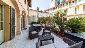 Un espace extérieur aménagé en terrasse, avec des meubles en osier, une table sur laquelle se trouvent une bouteille et des verres, ainsi que des plantes en pot.