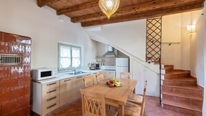 Une cuisine avec une table en bois, des chaises, un four à micro-ondes et un escalier menant à un autre niveau.